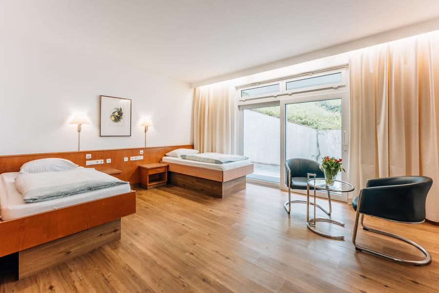 Großes Zimmer mit zwei Einzelbetten, zwei Stühlen und großer Balkontür