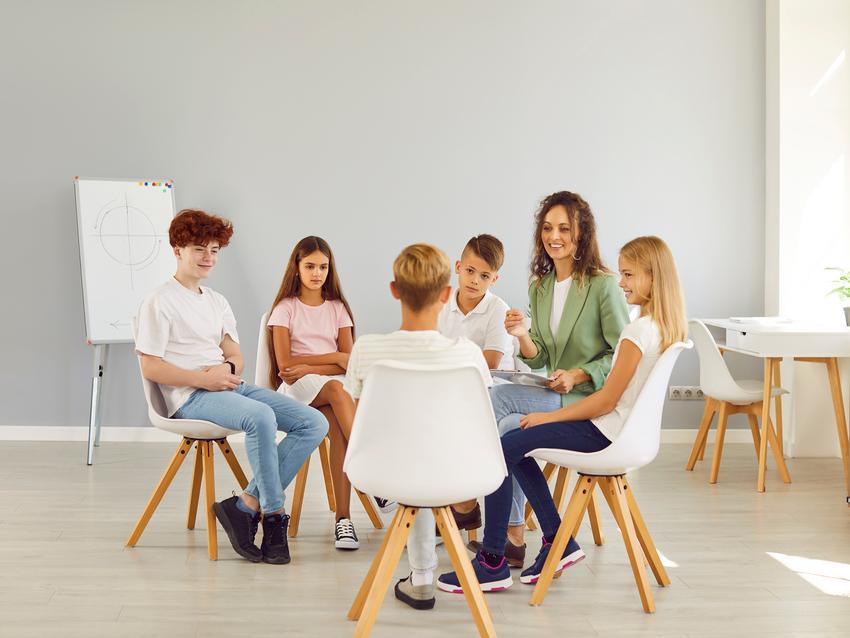 Kinder sitzen in einem hellen Raum in einem Stuhlkreis mit einer Therapeutin