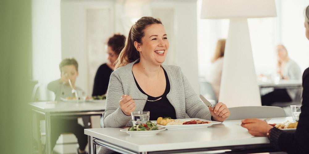 Eine junge blonde Frau sitzt an einem Tisch und lächelt während sie isst