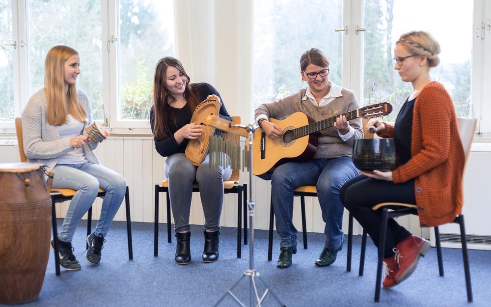 Vier Frauen sitzen in einem Stuhl-Halbkreis und halten jeweils ein Instrument