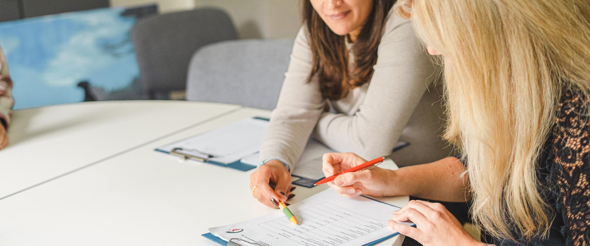 Zwei Frauen sitzen an einem Tisch über Dokumente gebeugt und unterhalten sich