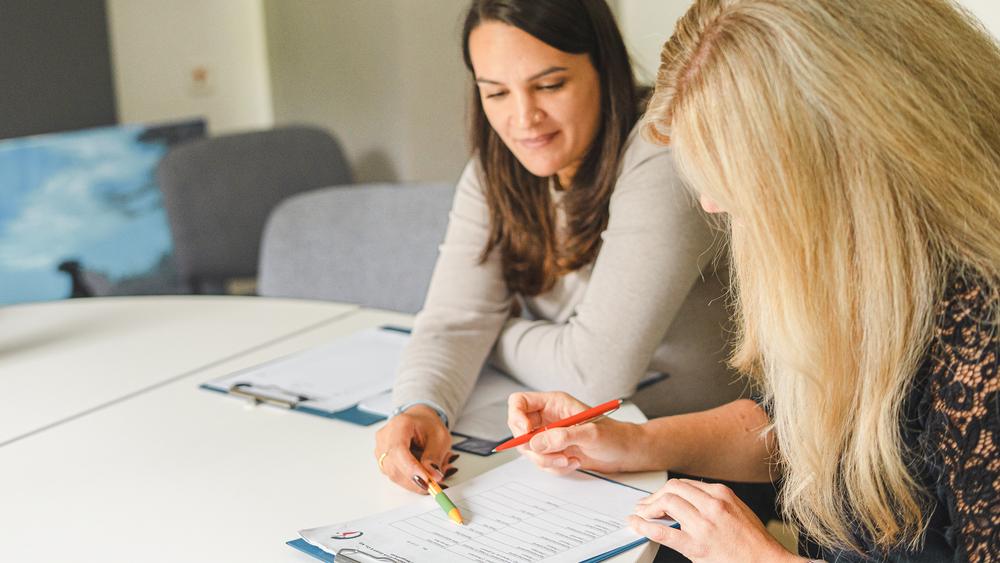 Zwei Frauen sitzen an einem Tisch über Dokumente gebeugt und unterhalten sich