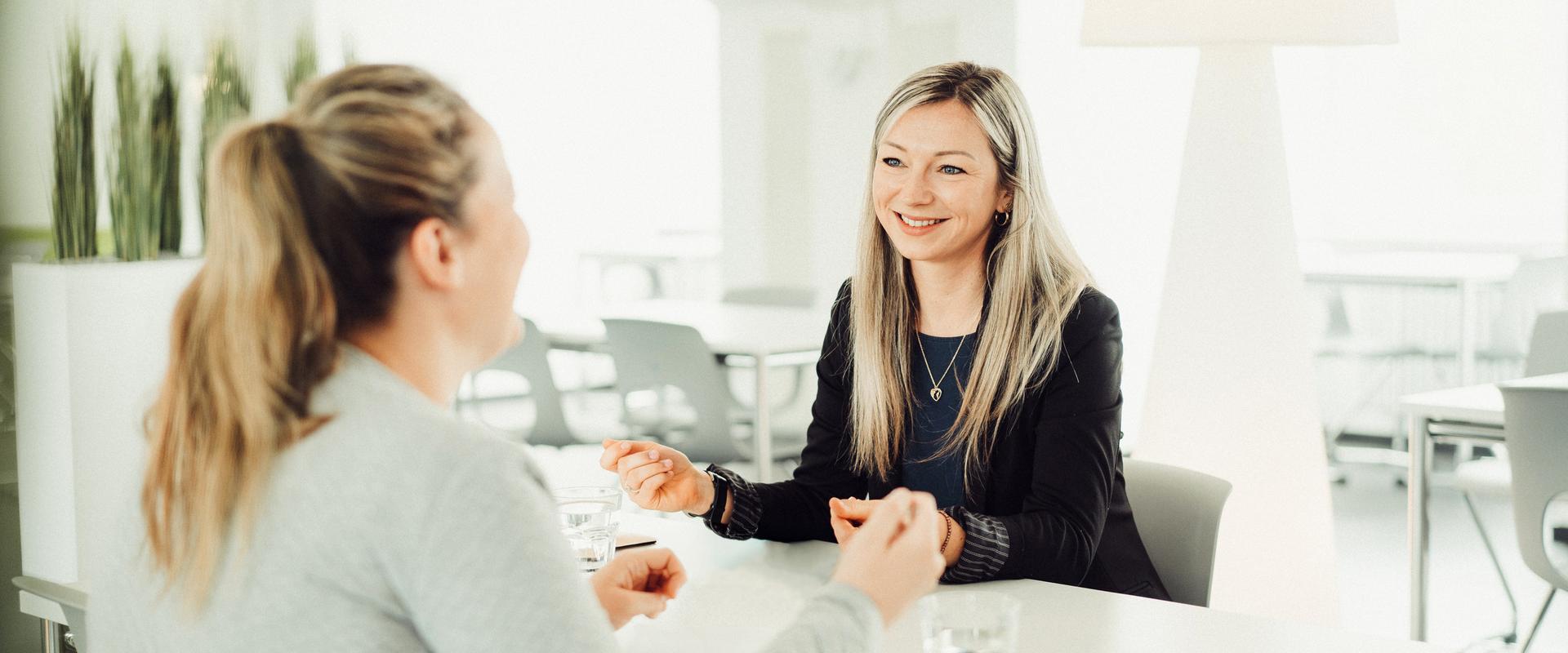 Zwei junge Frauen sitzen sich gegenüber und sprechen miteinander