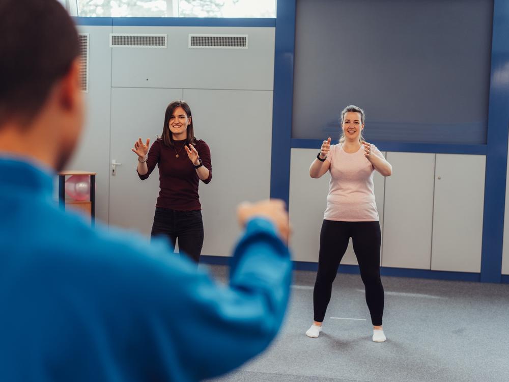 Zwei Frauen machen unter Anleitung eines Trainers sportliche Übungen im Bewegungsraum