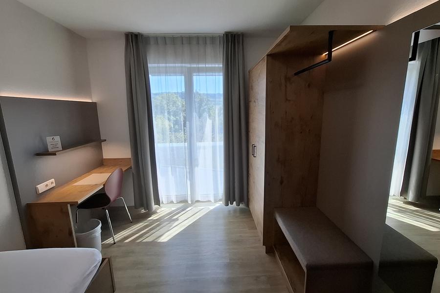 Modernes Zimmer mit Garderobe, Kleiderschrank, Schreibtisch und Balkontüren