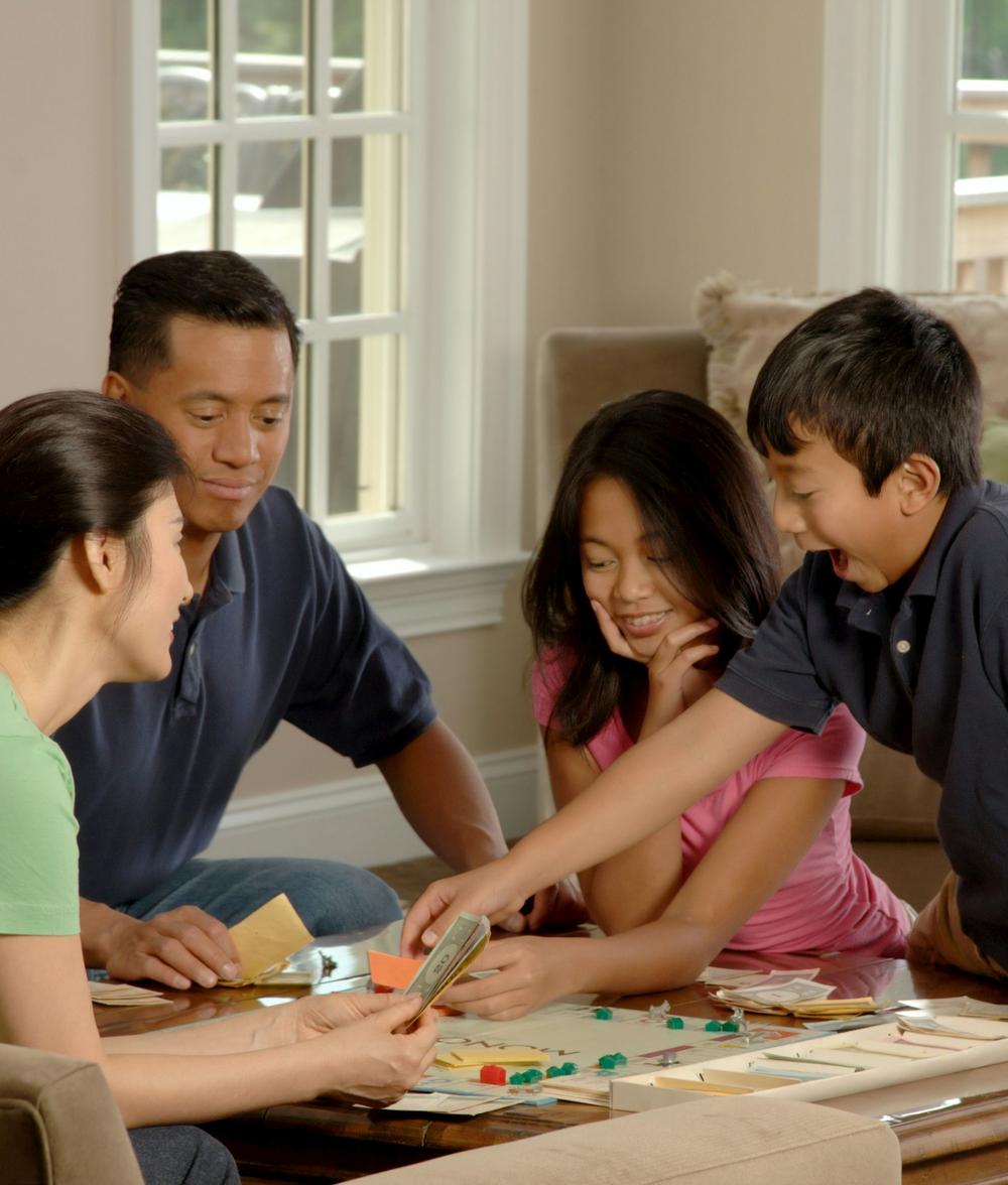Eine vierköpfige Familie sitzt an einem Tisch und spielt gemeinsam ein Brettspiel