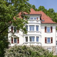 Weißes Akademiegebäude teils abgedeckt von umliegenden Bäumen
