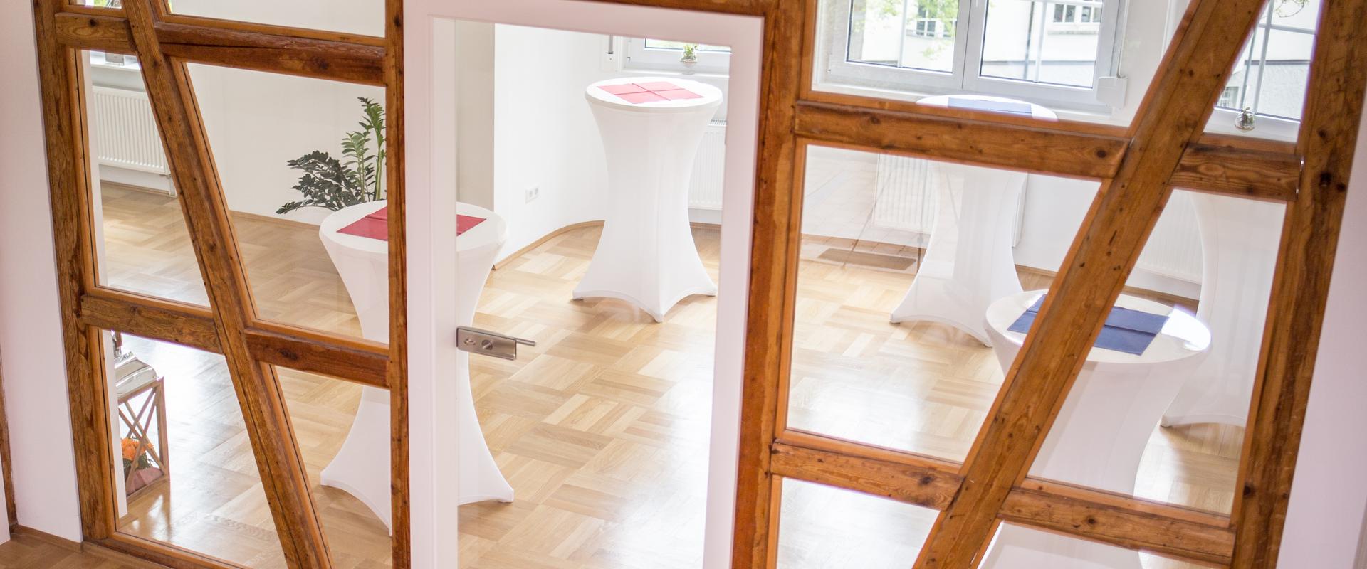 Offene Wand aus Holzbalken mit mehreren Stehtischen dahinter