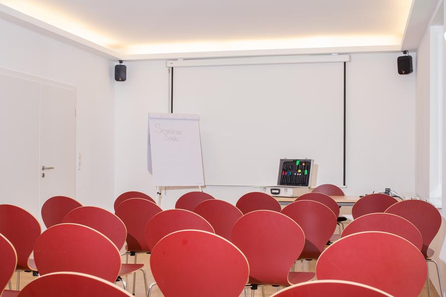 Mehrere rote Stühle in Reihen vor einem Whiteboard