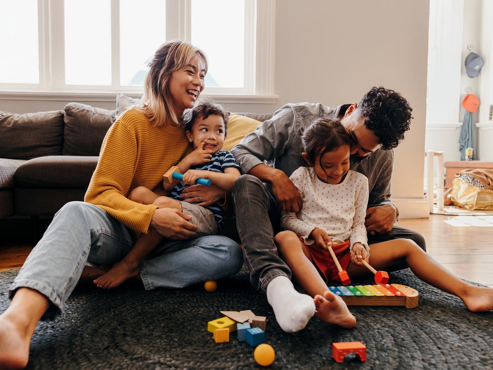 Eltern sitzen mit ihren zwei Kindern auf dem Boden zwischen Spielsachen und lachen